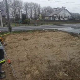 Przygotowany teren pod fundamenty z widocznymi śladami prac ziemnych i narzędziami pomiarowymi w tle zabudowa mieszkalna.