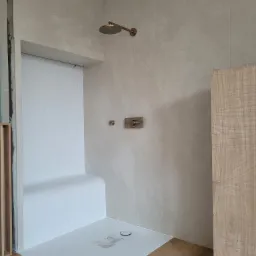 Nowoczesna kabina prysznicowa z siedziskiem wyłożonym mozaiką, armatura w kolorze miedzi, minimalistyczny design, drewnopodobna podłoga i okładzina ściany.