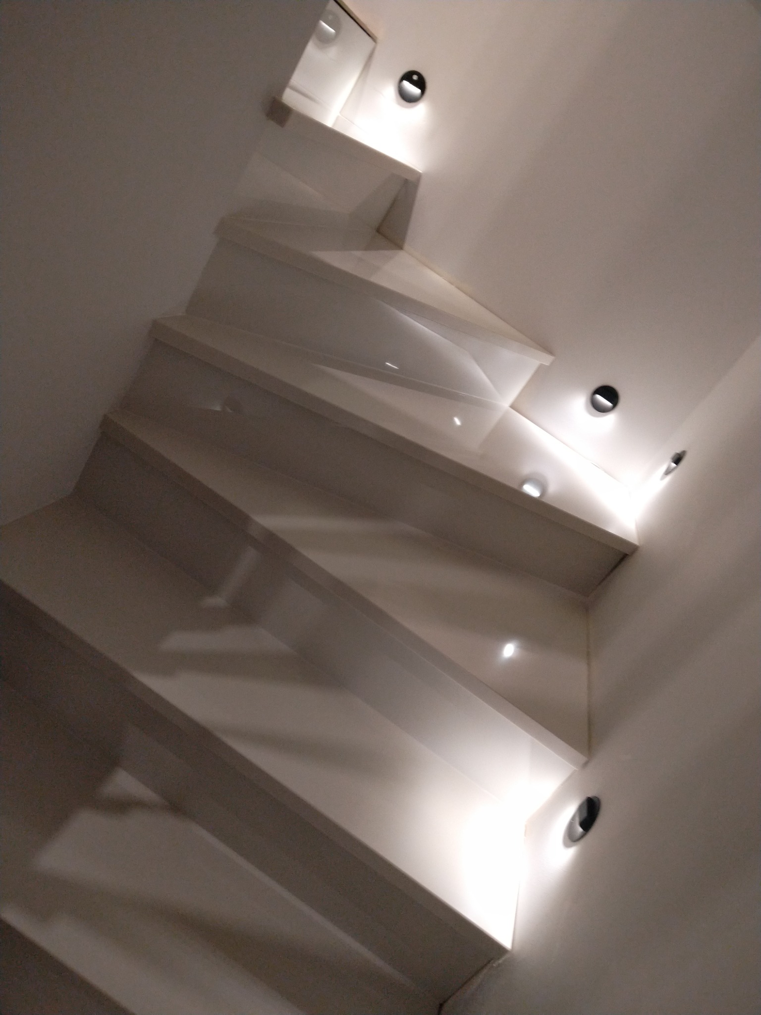 Nowoczesne białe schody z oświetleniem punktowym wbudowanym w ścianę, widok z dołu