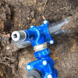 Yaroslav Khoronzhak - Niebieski zawór odcinający na czarnej rurze w wykopie ziemnym, widoczne połączenia śrubowe i nasadka z kwadratowym otworem.