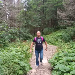 Mężczyzna z różowym plecakiem idzie kamienistą ścieżką przez gęsty las.