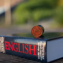 Stempel przysięgłego na słowniku angielsko-polskim na drewnianym stole, w tle rozmyta zieleń.