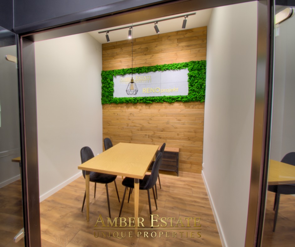 Jasne biuro z drewnianą ścianą, dekoracją z mchu, stołem z krzesłami i oświetleniem punktowym, widok z korytarza.