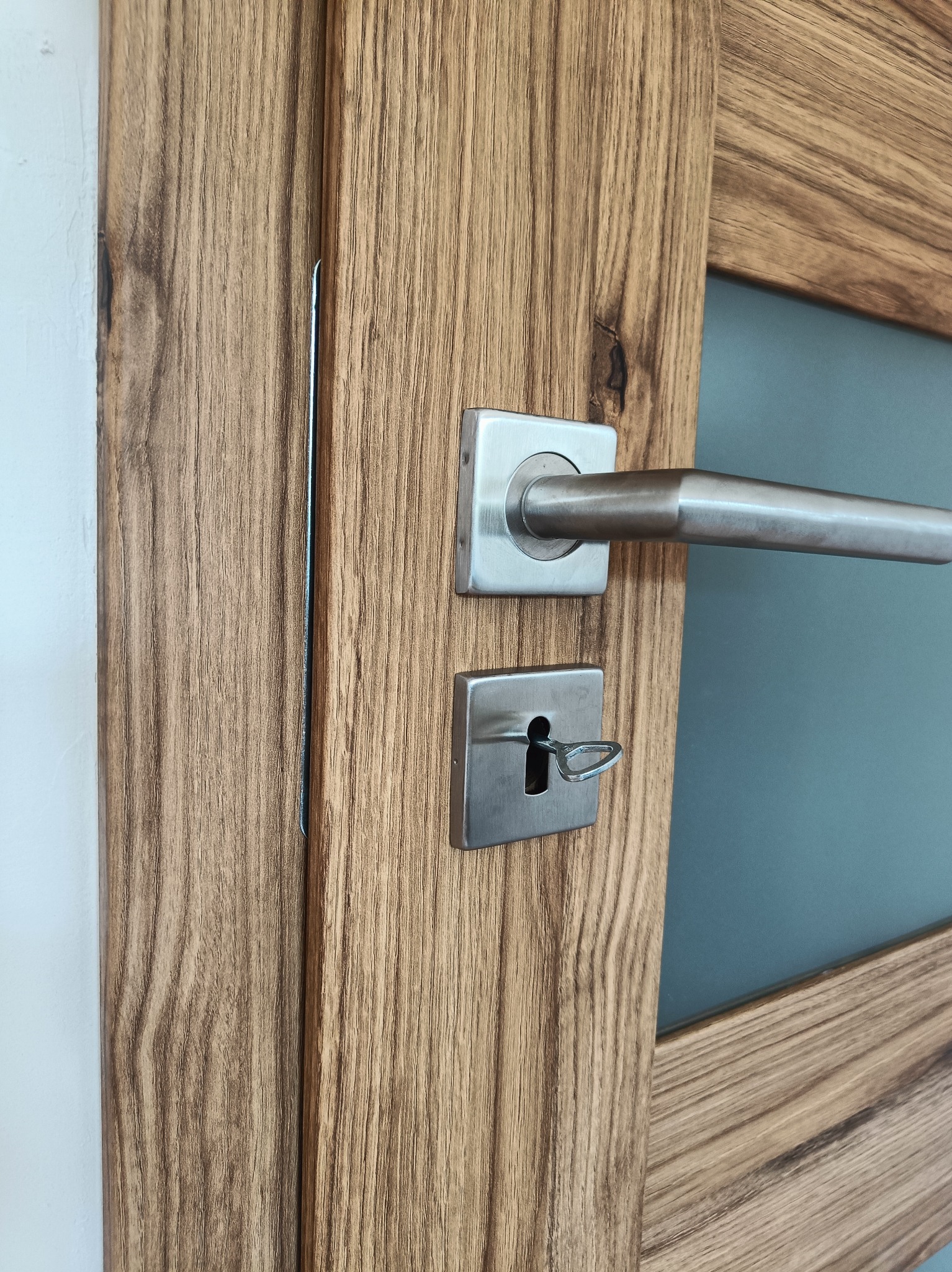 Zamknięte na klucz, drewniane skrzydło z przeszkleniem, zamontowane w Strzelcach Opolskich, z widoczną fakturą drewna i metalową klamką.