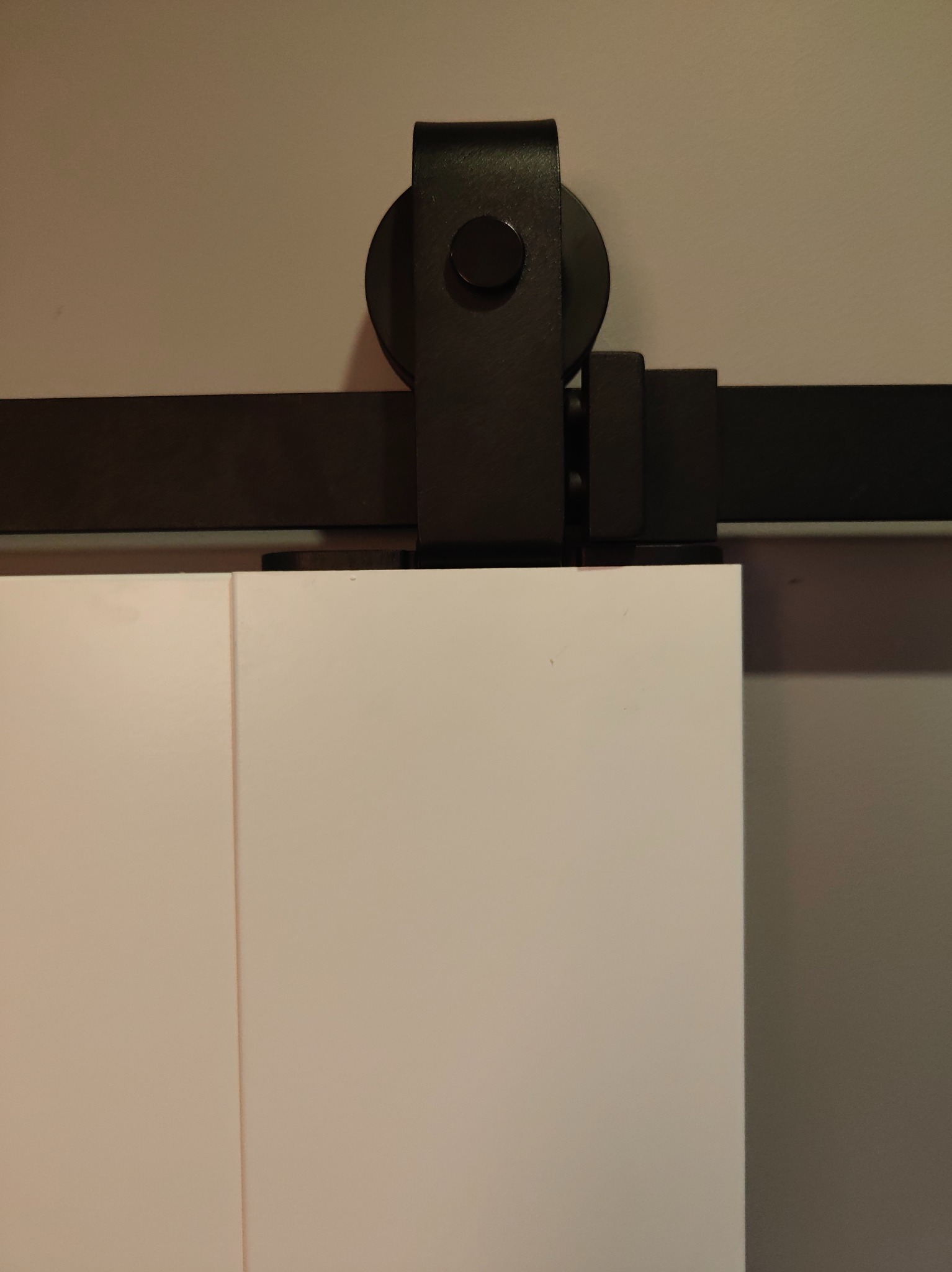 Białe drzwi przesuwne z czarnym, metalowym systemem prowadnic. Minimalistyczny design, widoczne detale mocowania i gładka powierzchnia drzwi.