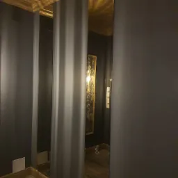 Wysokie lustra na ścianie w ciemnym pomieszczeniu z drewnianym sufitem i podłogą, złota rama lustra, widoczne odbicie obrazu.