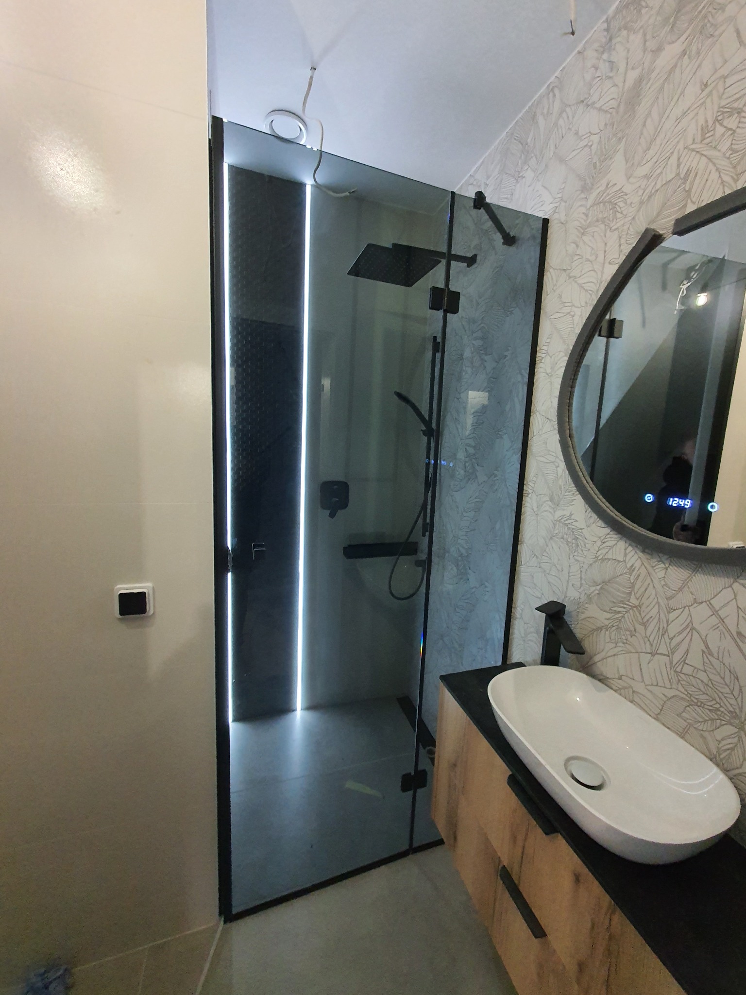 Nowoczesna kabina prysznicowa ze szklanymi ścianami i czarnymi profilami we Wrocławiu, widoczna umywalka nablatowa i lustro z podświetleniem LED.