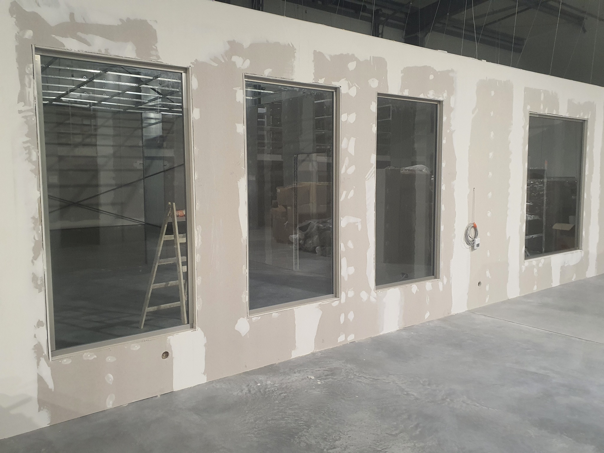 Montaż szklanych okien w ścianie działowej, widoczne ślady szpachlowania i drabina oparta o ramę okienną.