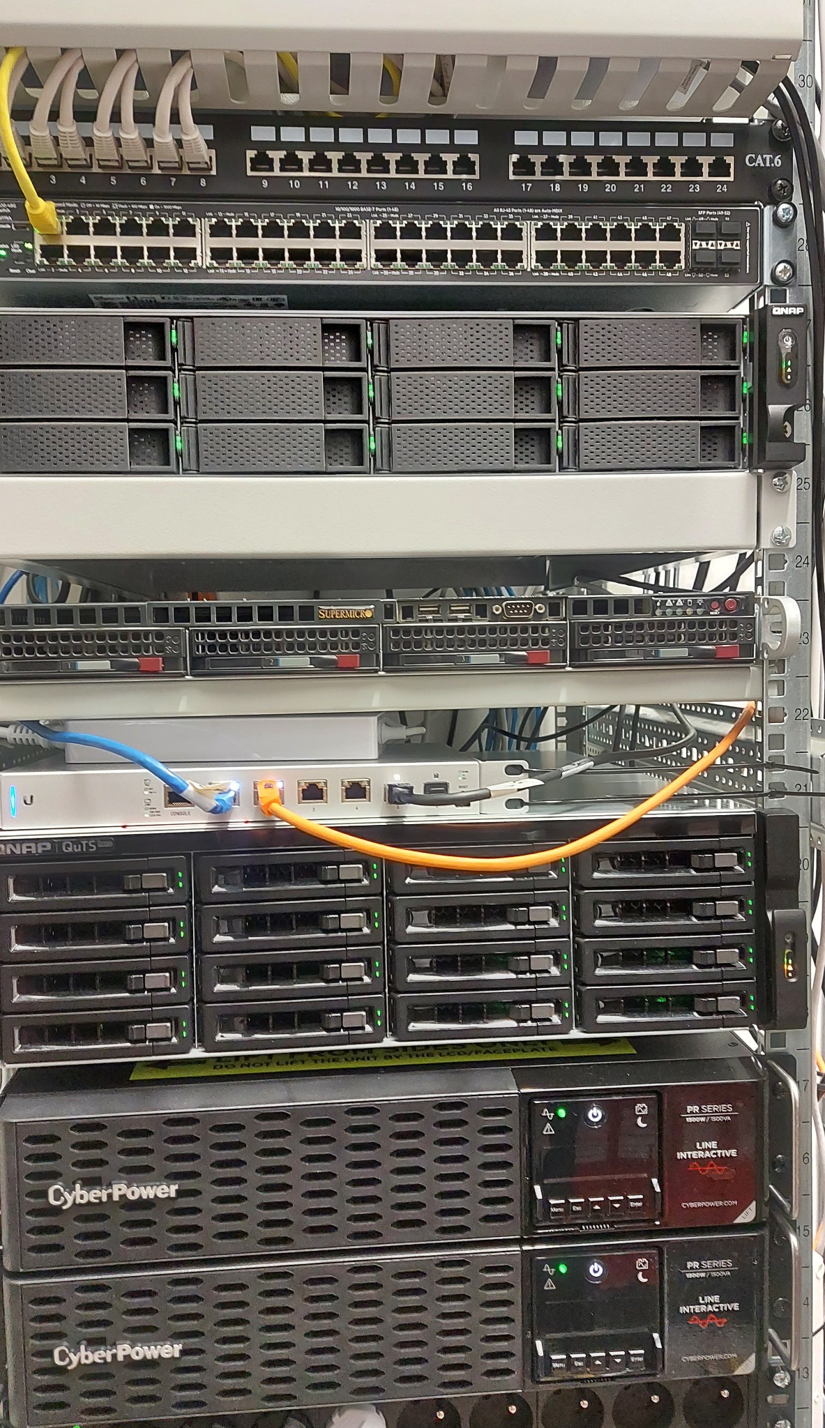 Szafa RACK z zamontowanym switchem, serwerami, zasilaczami awaryjnymi CyberPower i okablowaniem; widoczne porty RJ45 i diody sygnalizacyjne.