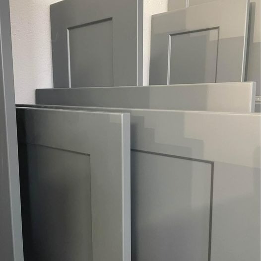 Stos szarych, lakierowanych frontów meblowych z frezowanymi ramkami, ułożonych jeden na drugim w warsztacie.