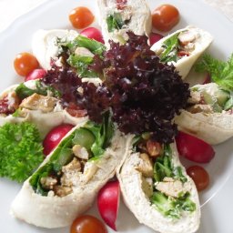 Ziółkowska-Don Carlos - Dekoracyjnie ułożone roladki z tortilli z kurczakiem, warzywami i serem, otoczone rzodkiewkami i pomidorkami cherry na białym talerzu.