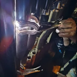 Metalowe rury mocowane zaciskiem przez osobę w rękawicach roboczych, widoczne ślady obróbki.