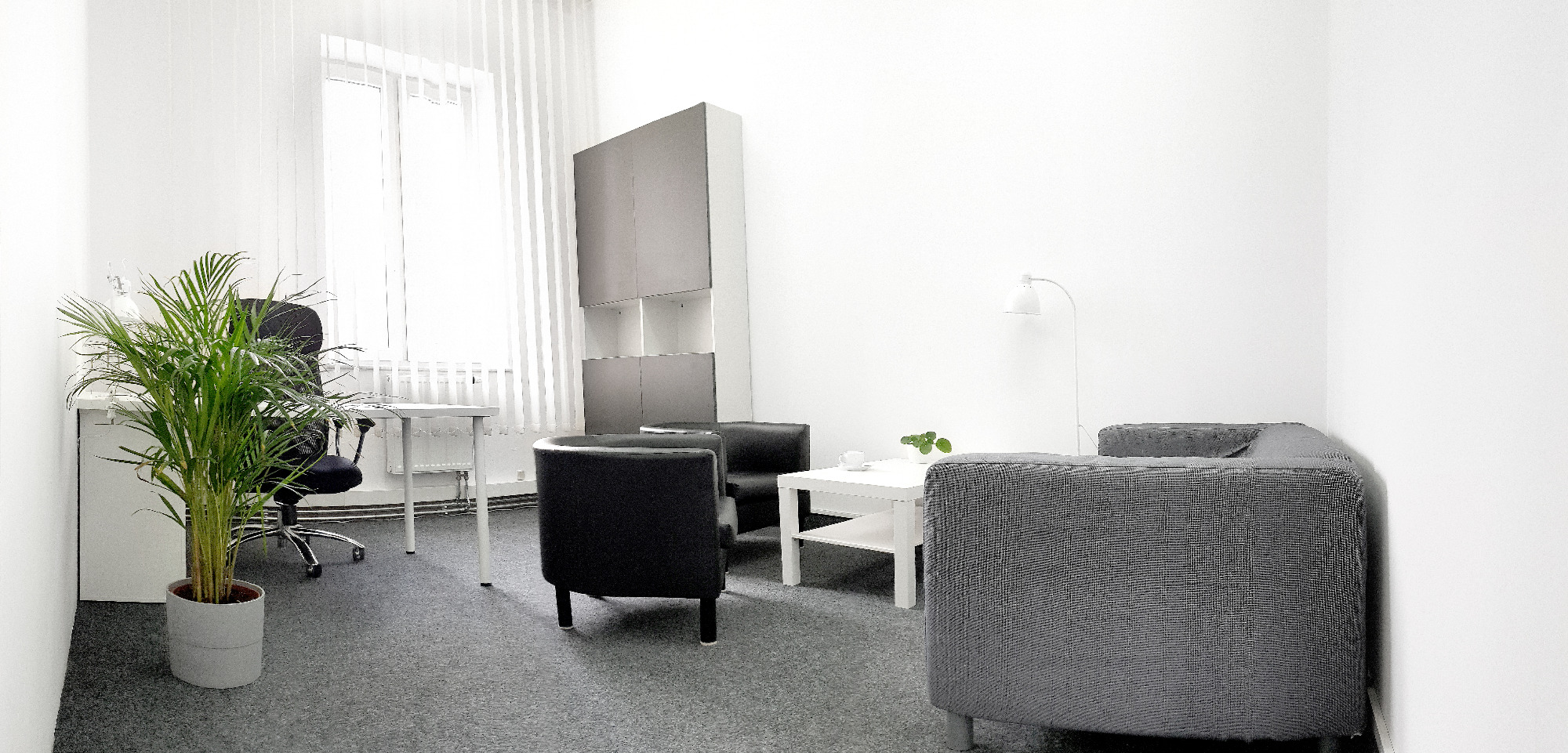 Jasne, minimalistyczne wnętrze gabinetu z biurkiem, krzesłem, rośliną doniczkową, sofą i stolikiem kawowym.