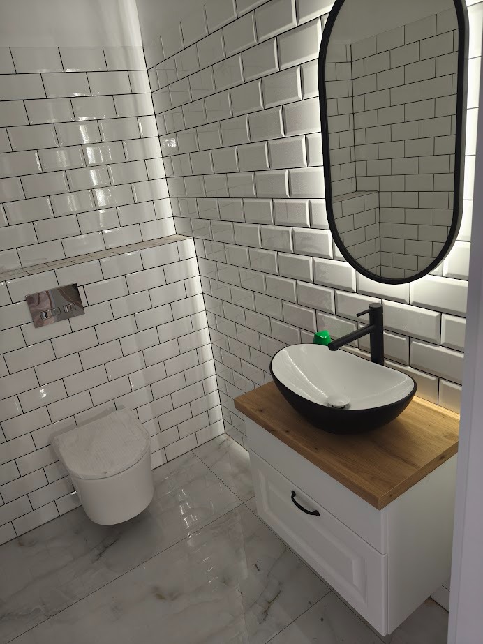 Nowoczesna łazienka: białe płytki metro, owalna umywalka na drewnianym blacie, czarna armatura i owalne lustro z podświetleniem LED.