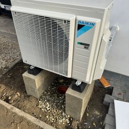 ECO CONNECT SPÓŁKA Z OGRANICZONĄ ODPOWIEDZIALNOŚCIĄ - Zewnętrzna jednostka pompy ciepła Daikin, model Inverter R32, zamontowana na betonowych blokach w przygotowanym wykopie. Widoczne elementy instalacji i otoczenie.