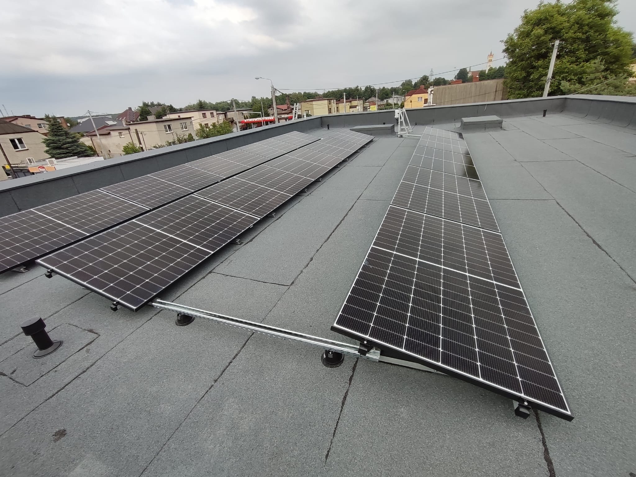 Panele słoneczne zamontowane na płaskim dachu budynku w Bytomiu, widoczne elementy montażowe i instalacyjne, w tle zabudowa miejska pod pochmurnym niebem.