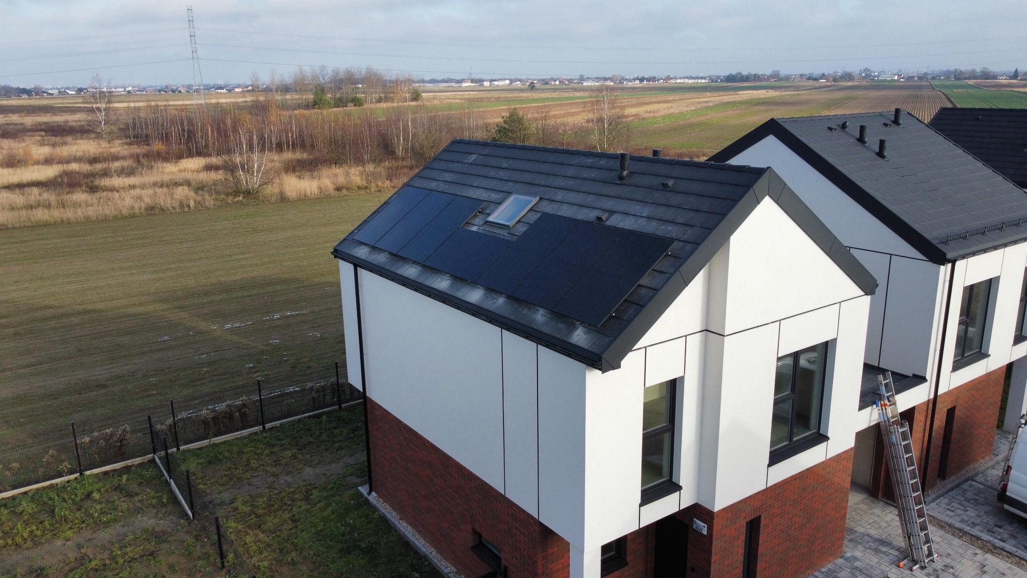 Nowoczesny dom z panelami słonecznymi na dachu, widok z góry. Czysta energia w architekturze, krajobraz wiejski w tle. Dachówka w kolorze antracytu.