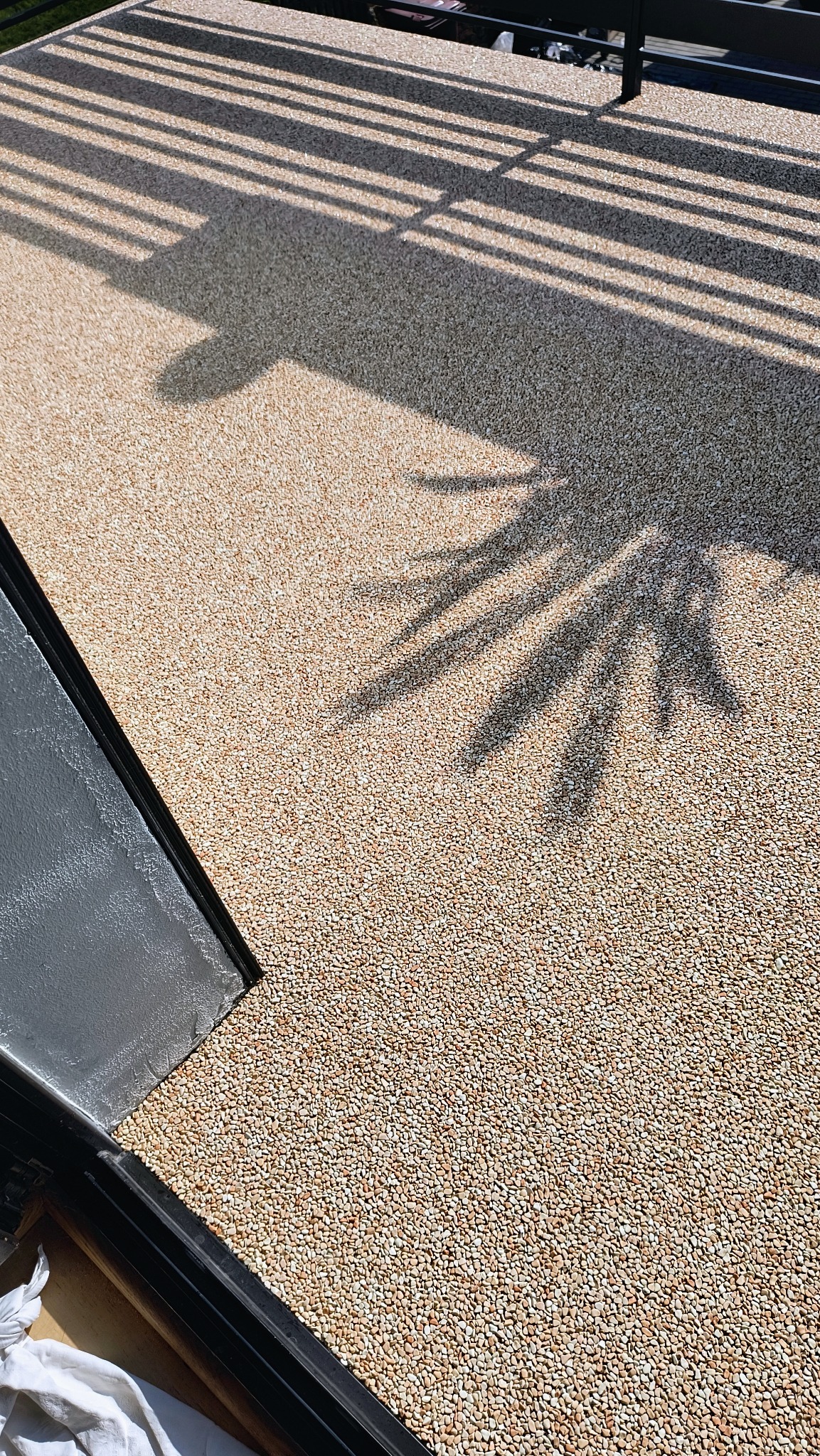 Jasna, drobnoziarnista powierzchnia z żywicy epoksydowej w Jarocinie, oświetlona słońcem i zacieniona przez metalową konstrukcję balkonu oraz liście drzewa.