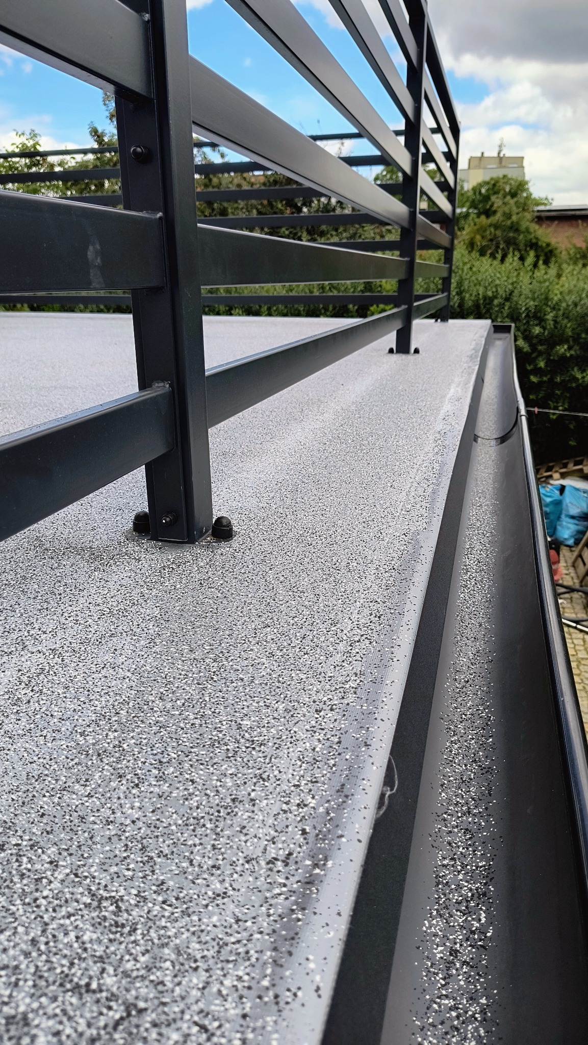 Szara, drobnoziarnista powierzchnia tarasu z metalową balustradą, widok z góry na zewnątrz.