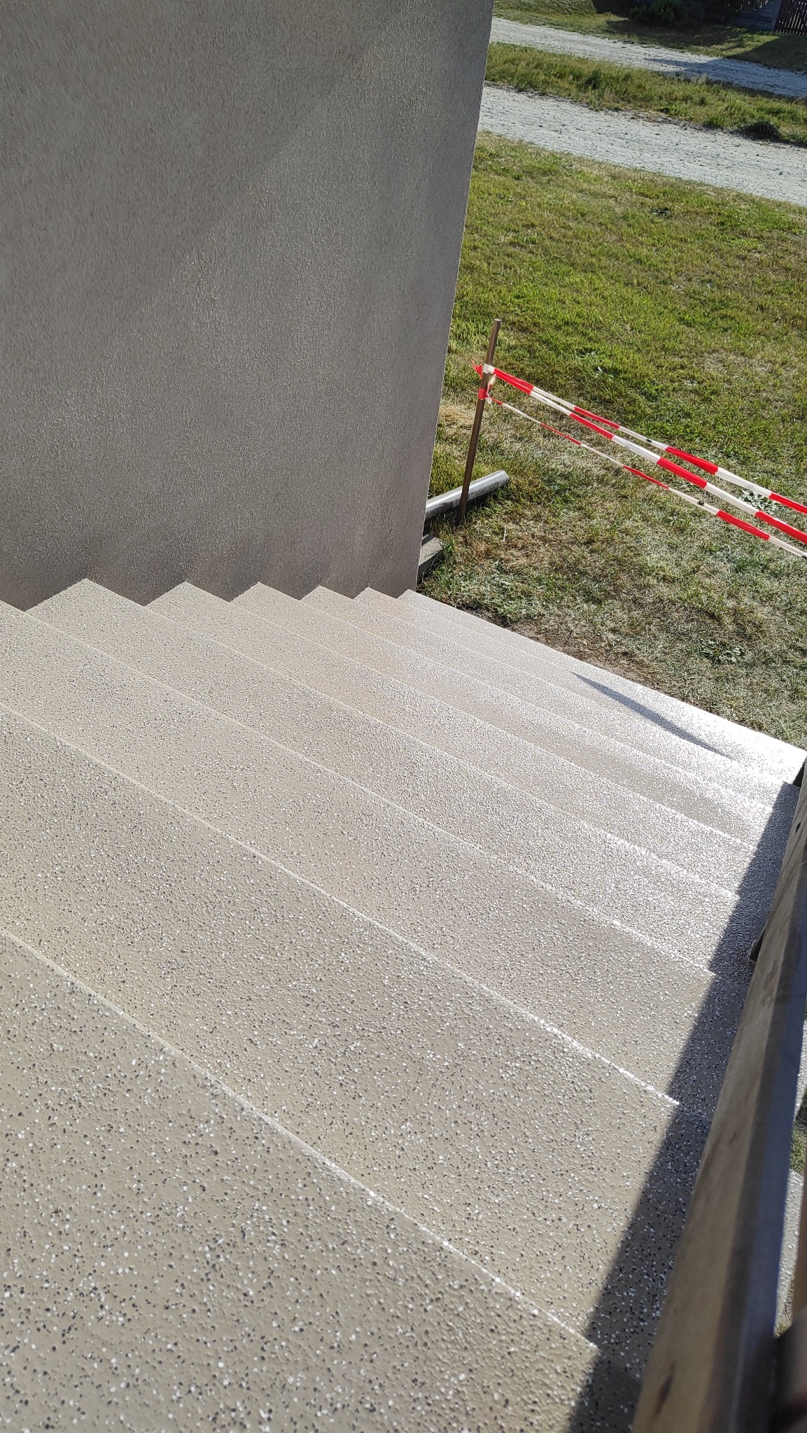 Schody zewnętrzne pokryte jasną, szarą, chropowatą powłoką, zabezpieczone czerwoną taśmą ostrzegawczą, widok z góry.