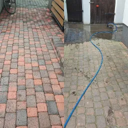 Częściowo umyta kostka brukowa przed garażami, widoczna różnica w kolorze między czystą a brudną powierzchnią, niebieski wąż ciśnieniowy na mokrej kostce.