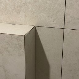 E-DOMIŚ - Beżowe, matowe płytki ceramiczne ułożone na ścianie i półce w łazience. Widoczne fugi i krawędzie płytek. Minimalistyczny design.