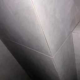 Szare, matowe płytki ceramiczne ułożone na ścianie pod kątem, widoczne fugi.