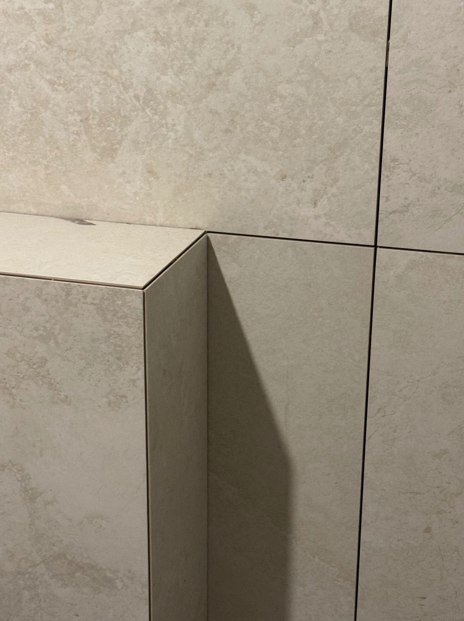 Beżowe, matowe płytki ceramiczne ułożone na ścianie i półce w łazience. Widoczne fugi i krawędzie płytek. Minimalistyczny design.