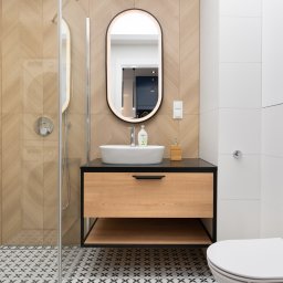 KONCEPT Nieruchomości - Nowoczesna łazienka z kabiną prysznicową, umywalką nablatową na szafce z drewnianym frontem, podświetlanym lustrem i wzorzystą podłogą.