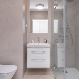 KONCEPT Nieruchomości - Nowoczesna łazienka w stonowanych beżach z kabiną prysznicową, umywalką z szafką, toaletą i pralką.