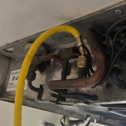 Ur serwis sp. Z o.o. - Podłączenie żółtego węża do miedzianych rurek wewnątrz urządzenia chłodniczego. Widoczne złącza i przewody elektryczne. Detal instalacji klimatyzacji.