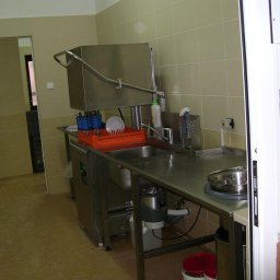 MEGAR Sp. z o.o. - Profesjonalna zmywarka tunelowa ze stali nierdzewnej w lokalu gastronomicznym, z widocznym koszem z umytymi naczyniami, zlewem i pojemnikiem na odpady pod blatem.