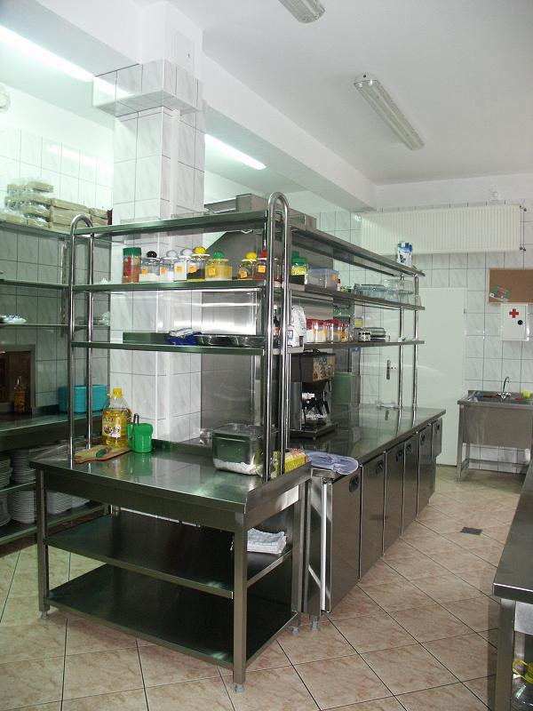 Profesjonalna kuchnia ze stali nierdzewnej z wyposażeniem, w tle białe płytki i oświetlenie jarzeniowe.