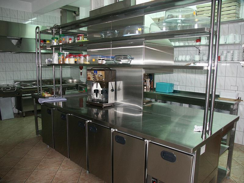 Profesjonalna kuchnia ze stali nierdzewnej z rzędami chłodziarek pod blatem, półkami z przyprawami i akcesoriami oraz ekspresem do kawy.