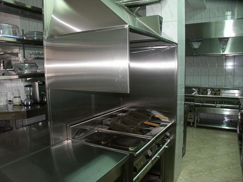 Profesjonalna kuchnia ze stali nierdzewnej z frytownicą, płytą grzewczą i okapem, widok z boku, płytki na ścianach.