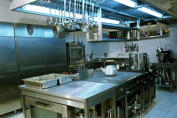 Profesjonalna kuchnia ze stali nierdzewnej w Zalesiu Górnym: duże chłodziarki, piec konwekcyjny, kuchenka gazowa z czajnikiem, wiszące przybory kuchenne i robot kuchenny.