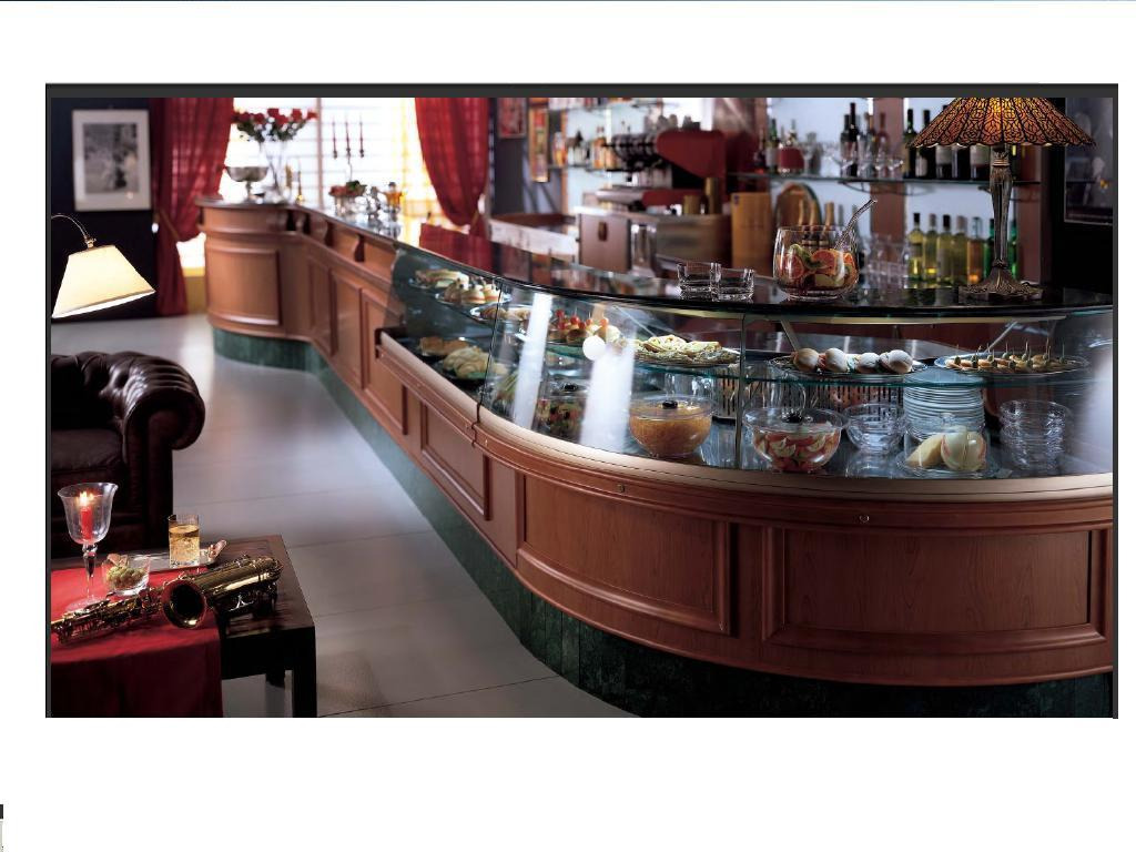 Elegancka lada chłodnicza z zakrzywioną szybą prezentująca dania i przekąski w restauracji o klasycznym wystroju, na pierwszym planie stolik z saksofonem i drinkiem.