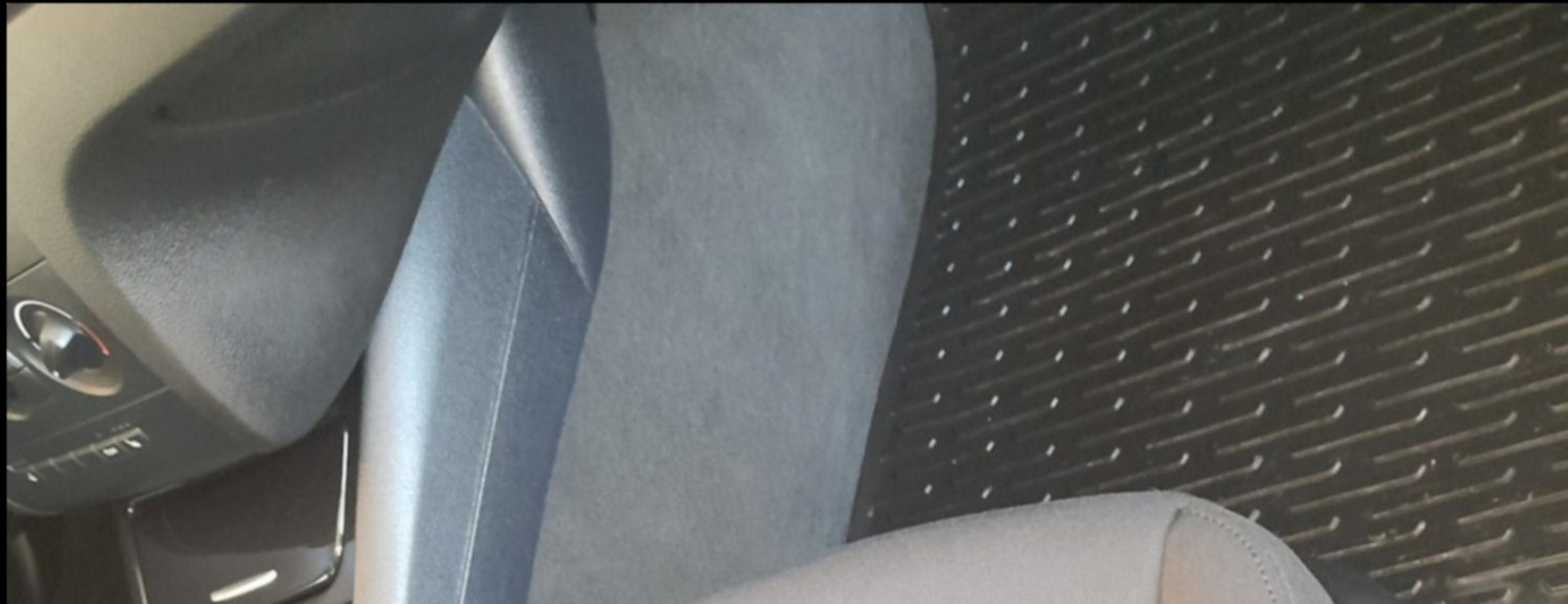 Wnętrze samochodu z szarą tapicerką fotela i gumową wycieraczką pod nogami pasażera z wzorem w ukośne linie.