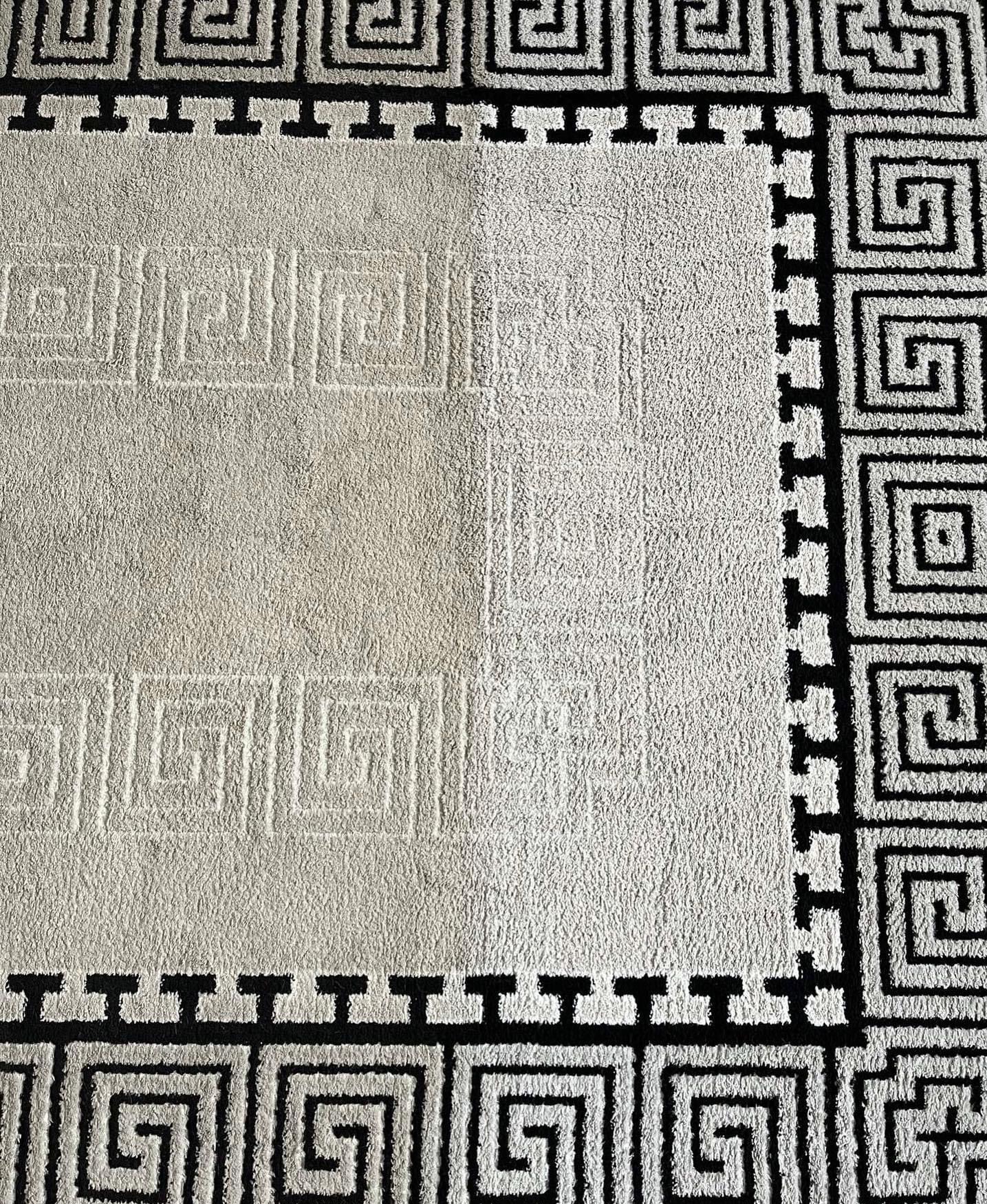 Fragment beżowego dywanu z czarnym geometrycznym wzorem w stylu greckim, widoczna różnica w czystości między wypraną a niewypraną częścią.