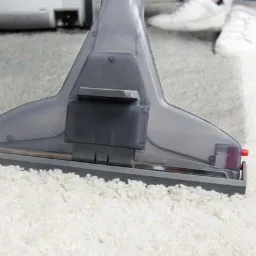 Szczegółowe ujęcie dyszy piorącej na białym, puszystym dywanie, z widoczną różnicą w czystości po lewej stronie, sugerującą trwający proces czyszczenia.