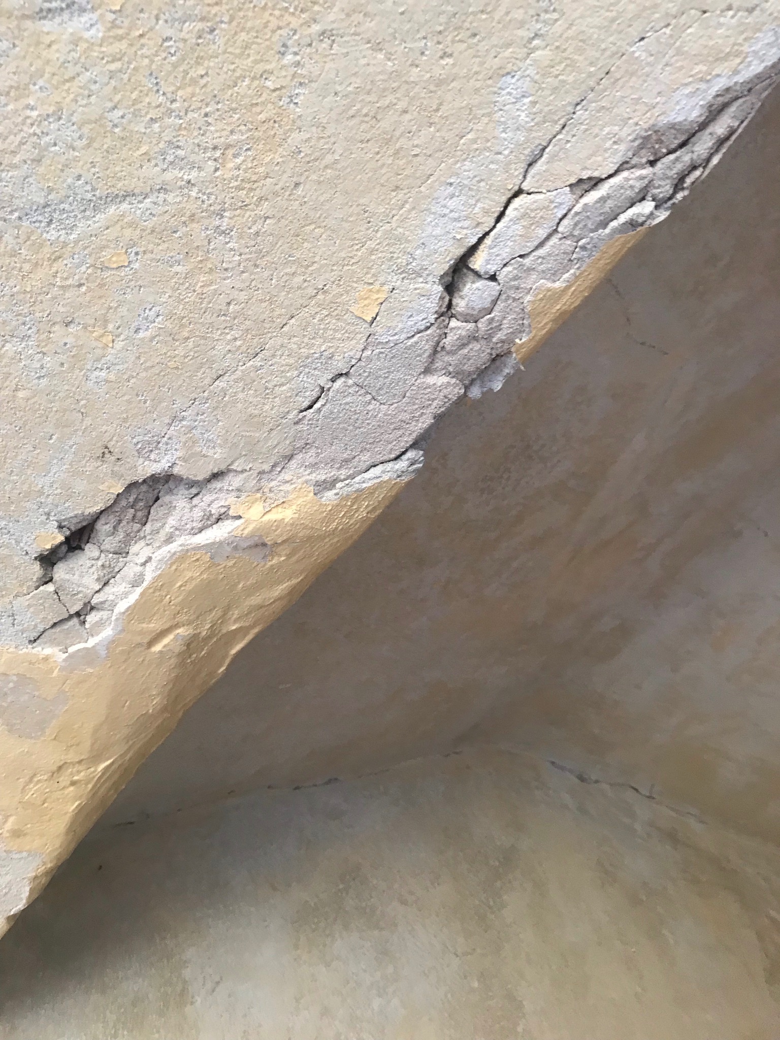 Pęknięcia i odspojenia farby na suficie w mieszkaniu, widoczne fragmenty starej, żółtej farby pod spodem.