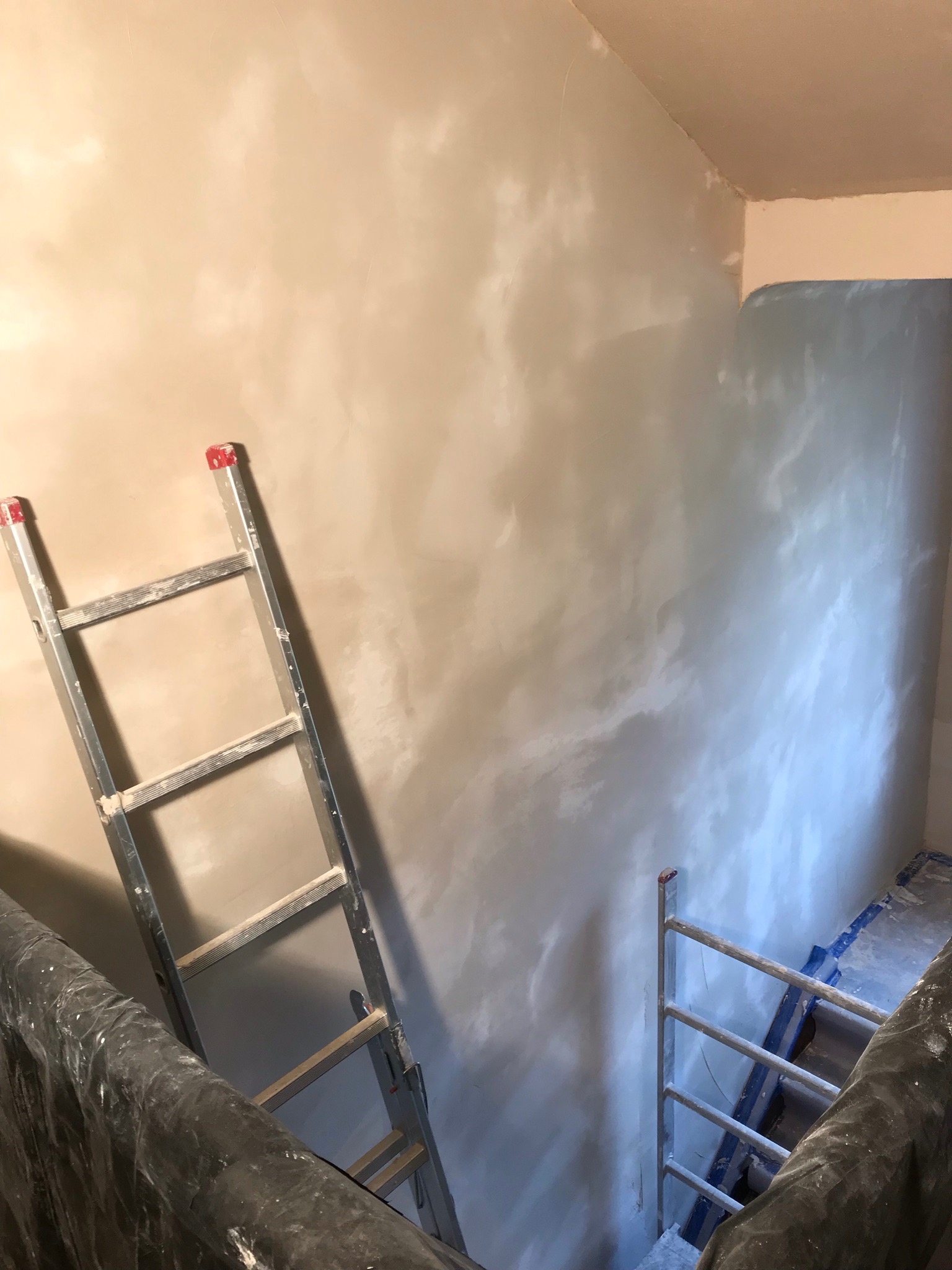 Ściana po malowaniu z efektem chmur, widoczna drabina aluminiowa z resztkami farby, zabezpieczone folią elementy pomieszczenia.