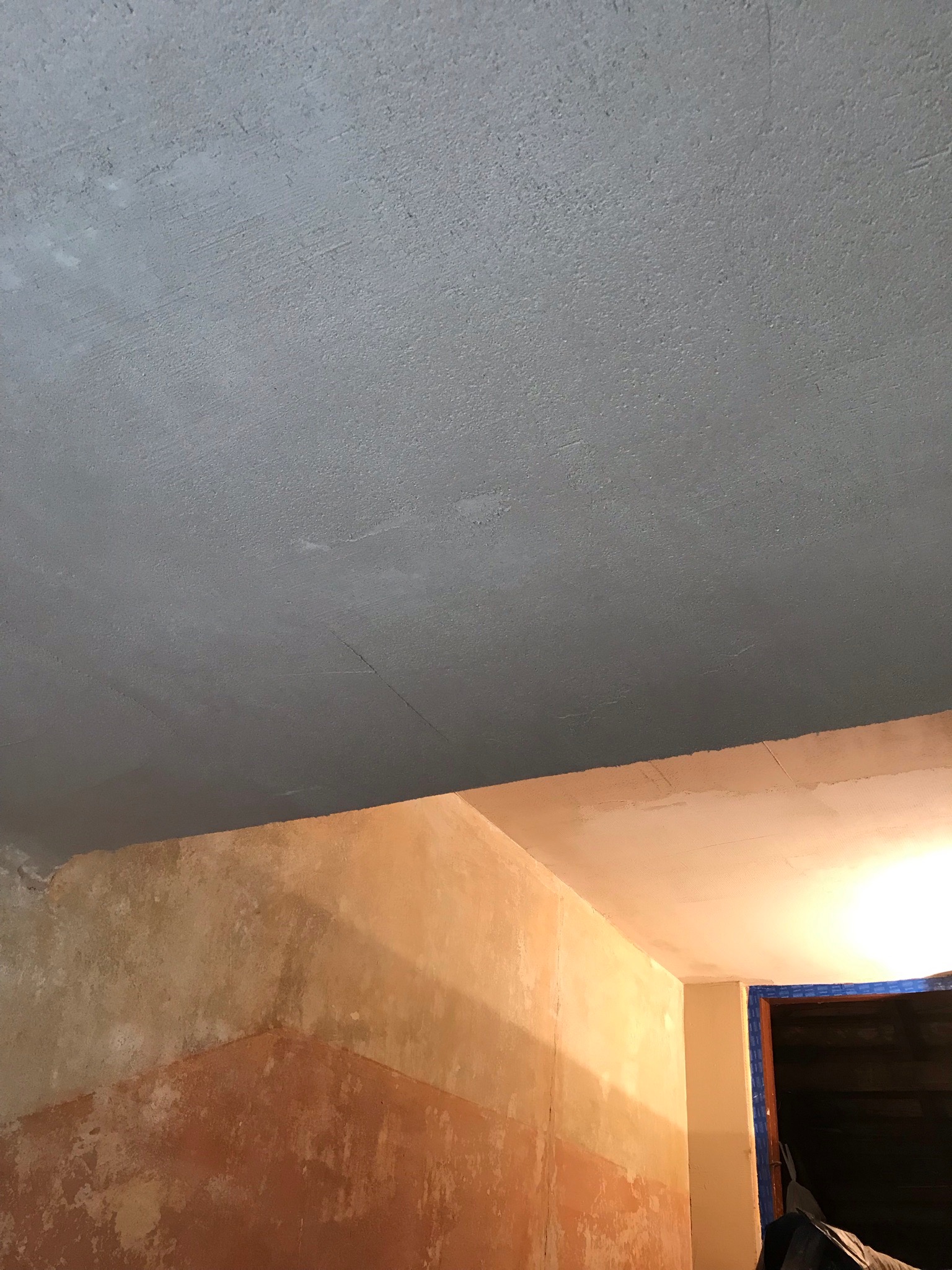 Szare, świeżo pomalowane sufity i ściany w trakcie remontu, widoczne niedoskonałości i różnice w odcieniach farby.