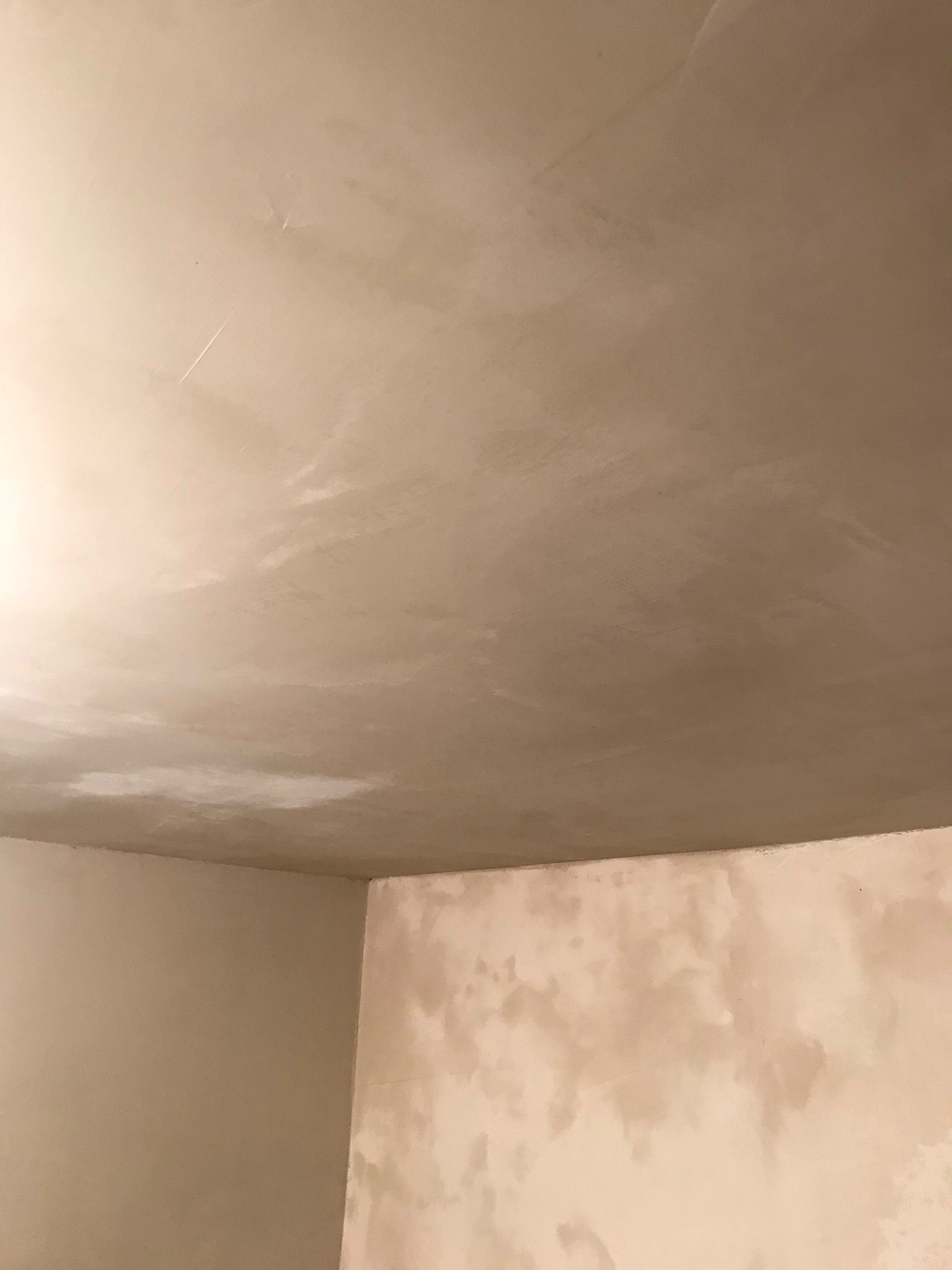 Niedokończone szpachlowanie sufitu i ściany w rogu pomieszczenia, widoczne nierówności i plamy szpachli.