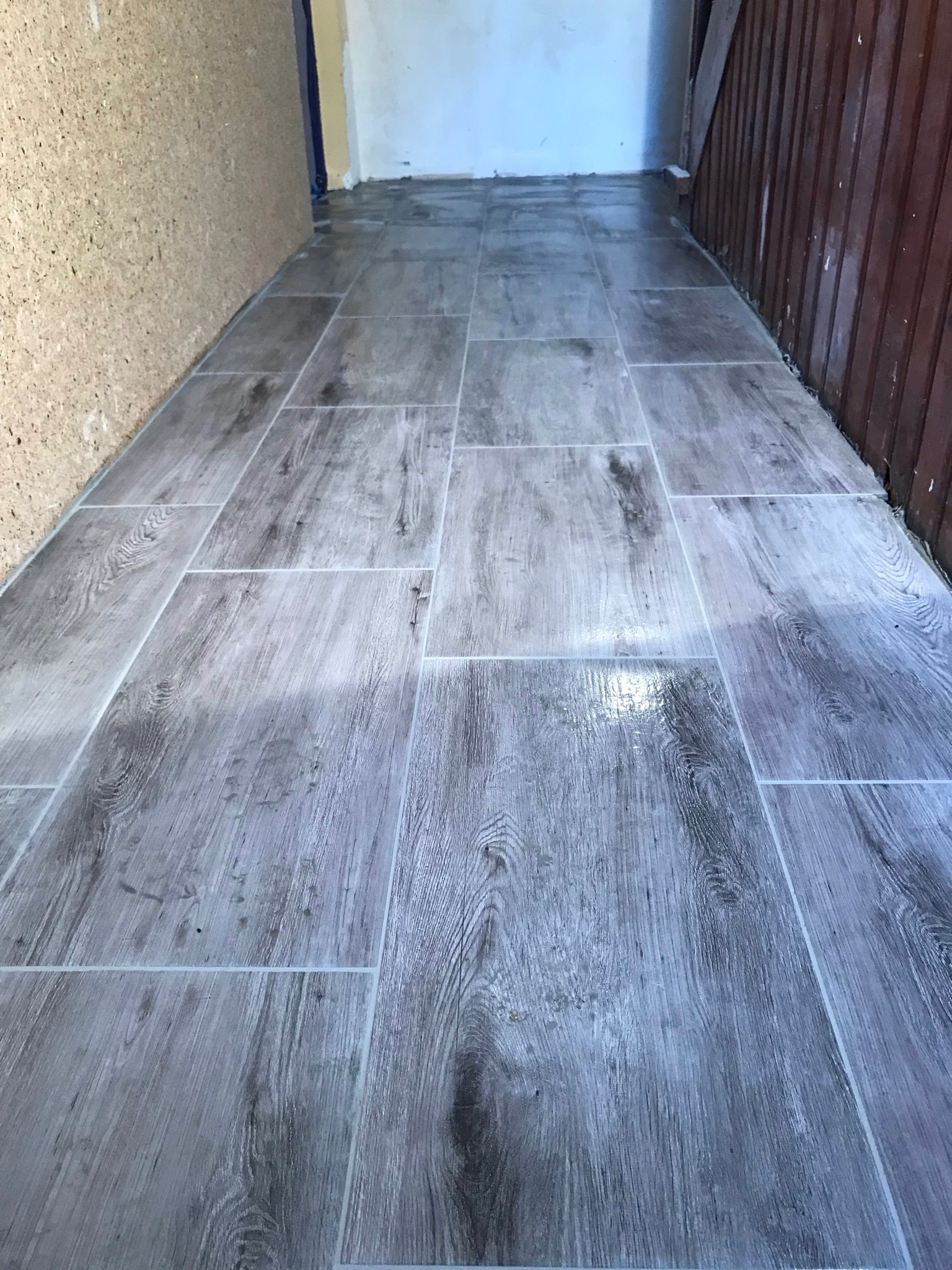 Świeżo ułożona podłoga z płytek imitujących drewno, widoczne drobne zabrudzenia po montażu przy ścianach z boazerią i korkiem.