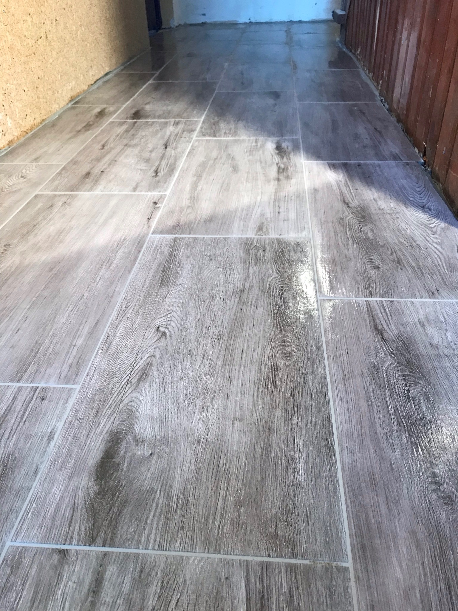 Świeżo ułożona, błyszcząca podłoga z płytek imitujących drewno w odcieniach szarości, z widocznymi fugami, w pomieszczeniu w trakcie wykańczania.