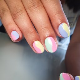 Beauty Center - Dłoń z pomalowanymi paznokciami w pastelowych kolorach: różowym, fioletowym, żółtym i miętowym, tworzącymi wzór fali na każdym paznokciu.