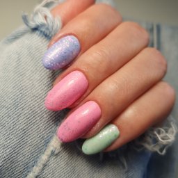 Beauty Center - Dłoń z pastelowymi paznokciami w odcieniach różu, błękitu i zieleni, ozdobionymi brokatem, na tle podartego denimu.