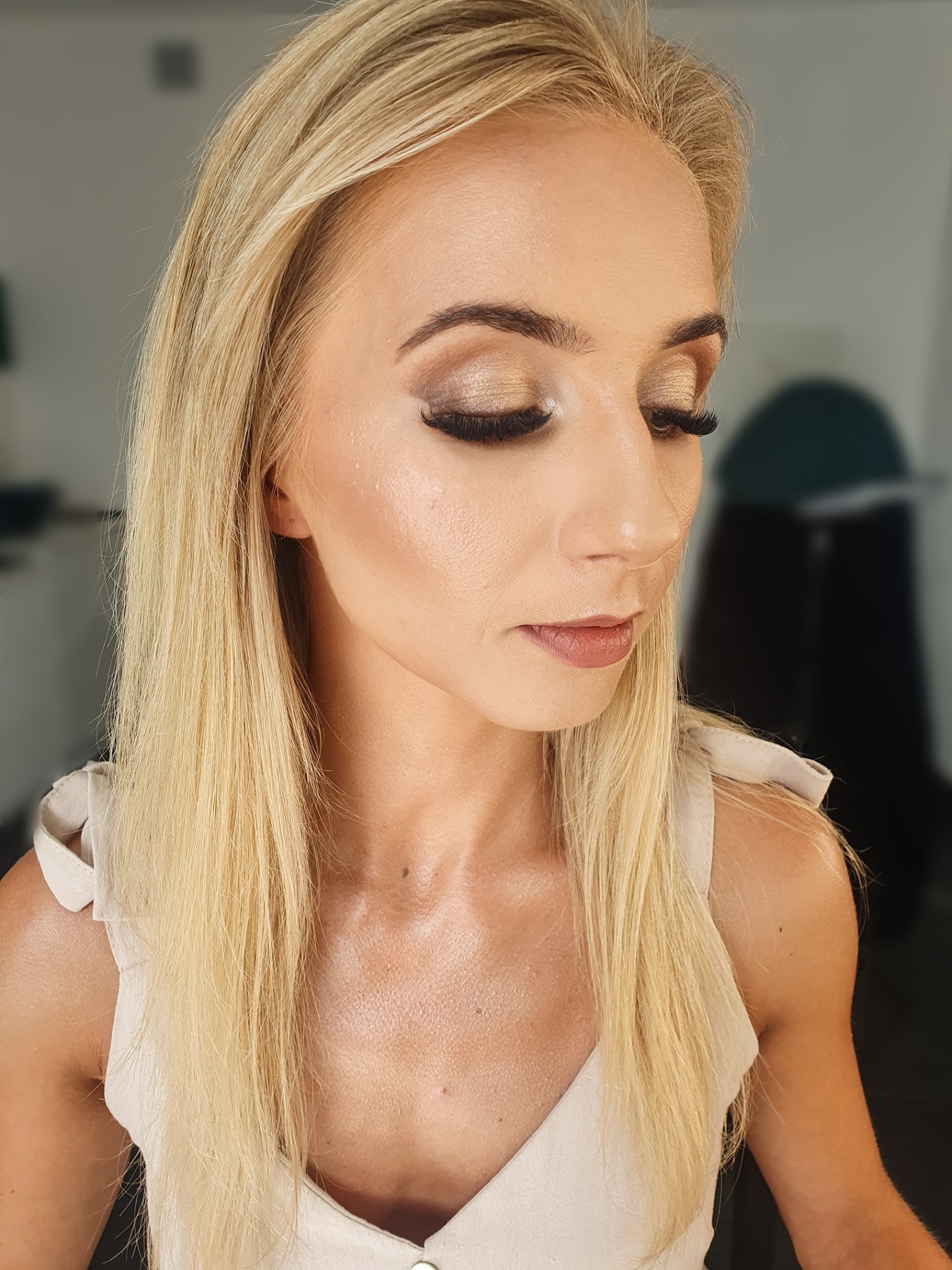 Portret kobiety z blond włosami i profesjonalnym makijażem oczu w odcieniach złota i brązu, z wyraźnie podkreślonymi rzęsami, delikatnym makijażem ust i subtelnym konturowaniem twarzy...