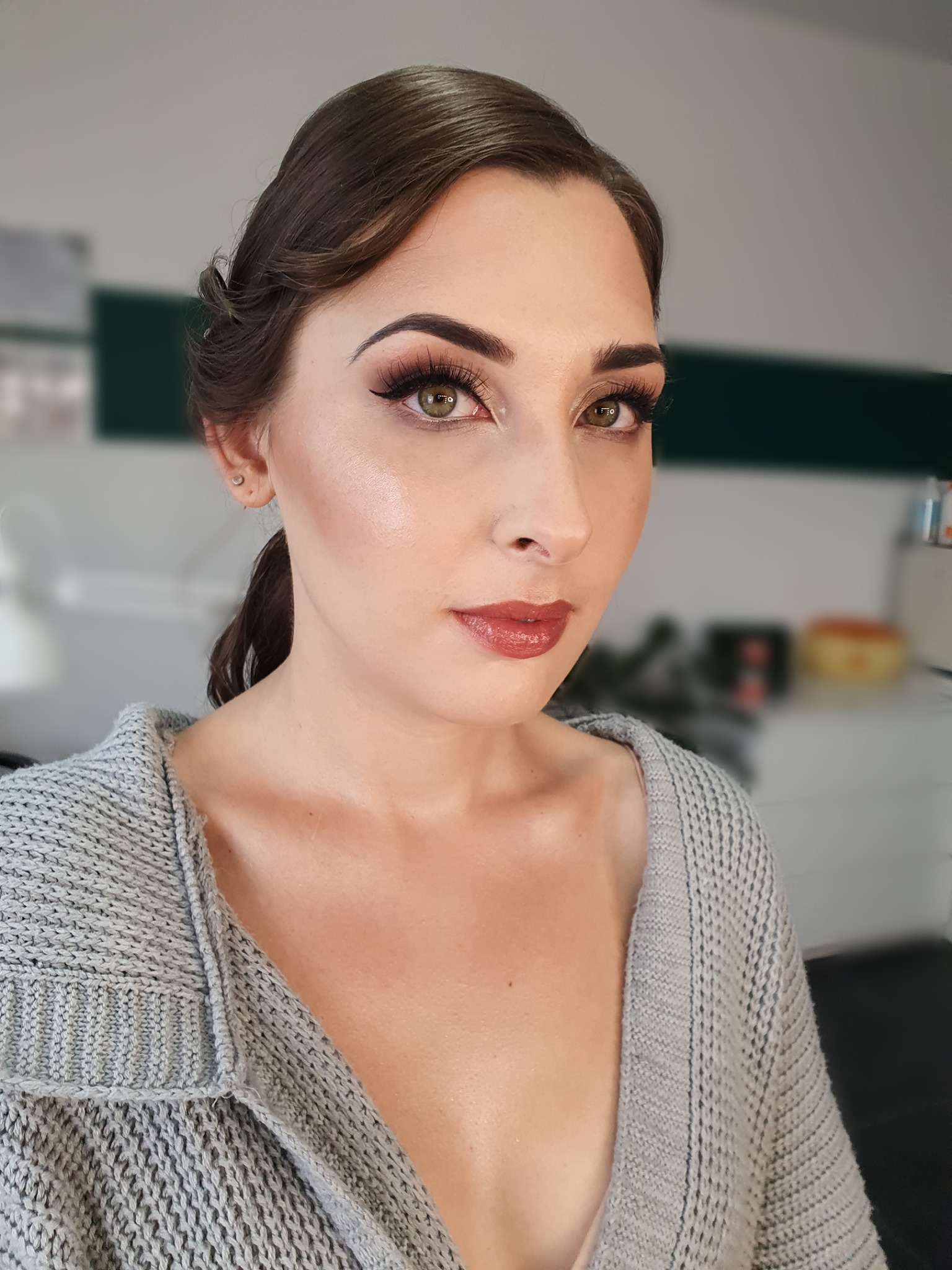 Portret kobiety z profesjonalnym makijażem, widoczne precyzyjne kreski na powiekach, rozświetlona cera i błyszczące usta w odcieniu brązu, włosy upięte w elegancki kok.